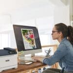 Une femme assise à un bureau, concentrée sur son travail, avec une imprimante Xerox® C320 couleur