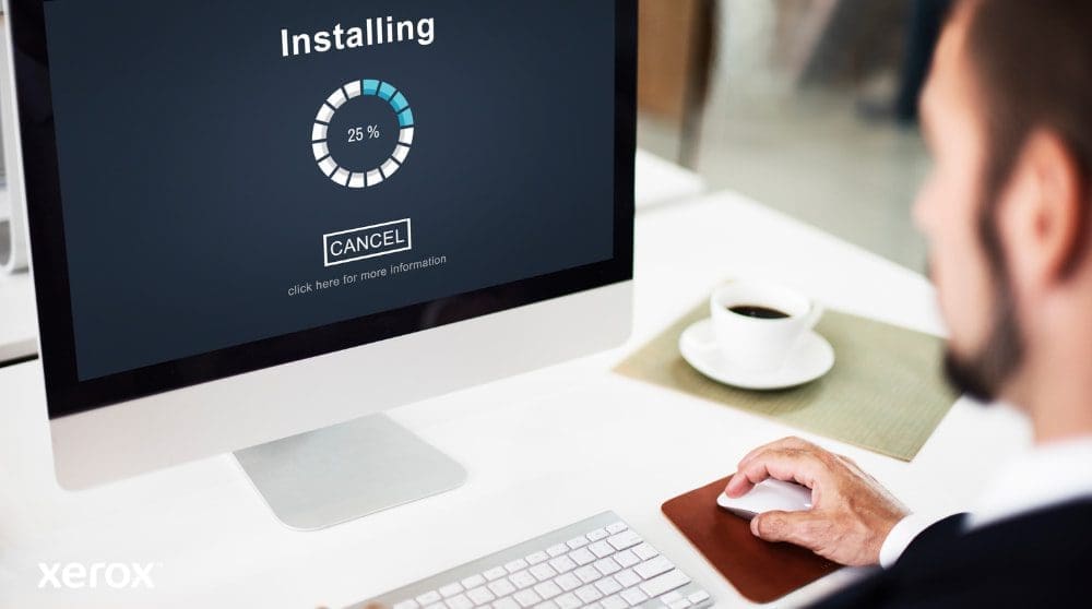 Vue rapproch&eacute;e d'un &eacute;cran d'ordinateur affichant une barre de progression &laquo; Installation &raquo; &agrave; 25 %, avec la main d'une personne sur une souris d'ordinateur &agrave; c&ocirc;t&eacute; d'une tasse &agrave; caf&eacute;, illustrant une configuration logicielle facile.